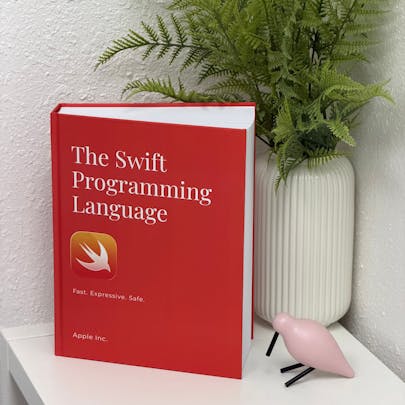 Photo of The Swift Programming Language as a physical print textbook. The cover is red. The book is propped up on a flat surface.