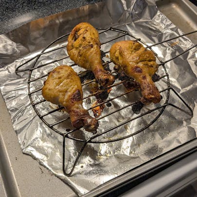 Three fully cooked tandoori chicken drumsticks with charred edges and golden-brown skin.