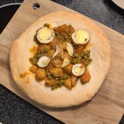 A top-down picture of a pizza with egg curry leftovers. The egg curry also has potatoes and peas.