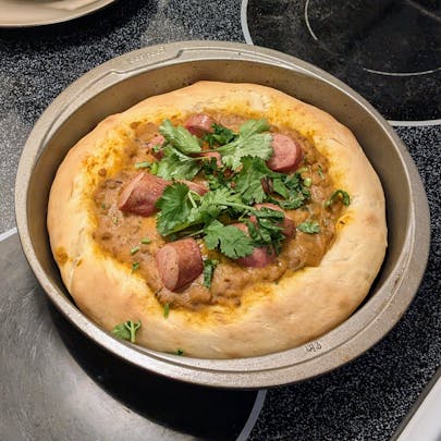 Freshly baked daal pizza, topped with sliced wieners and a generous cilantro.